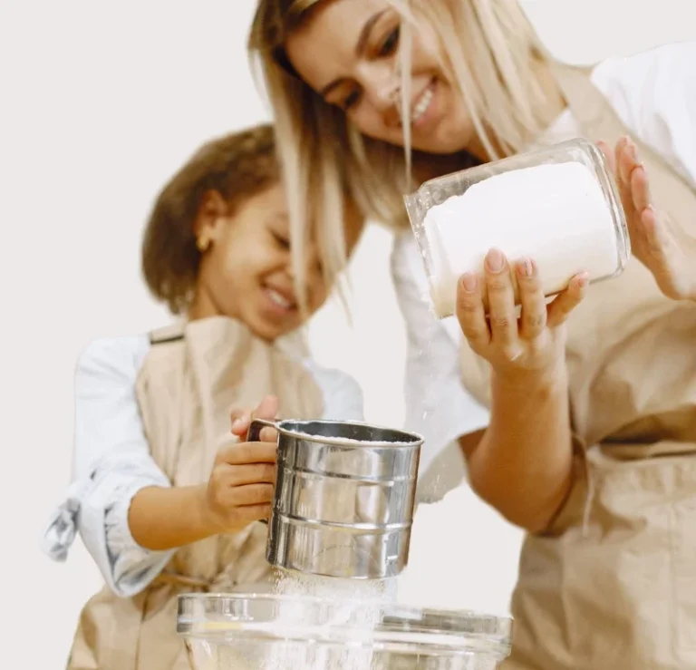 Eine Frau und ein Kind, beide in Schürzen, messen Zutaten in einer Schüssel ab.