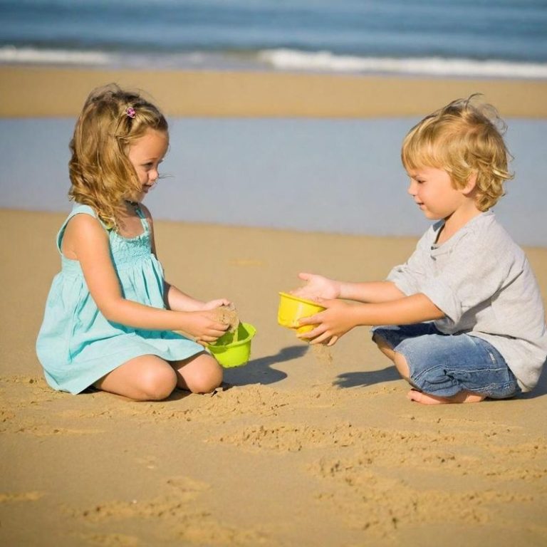 Zwei Kinder spielen am Strand und halten Sandschalen in der Hand.