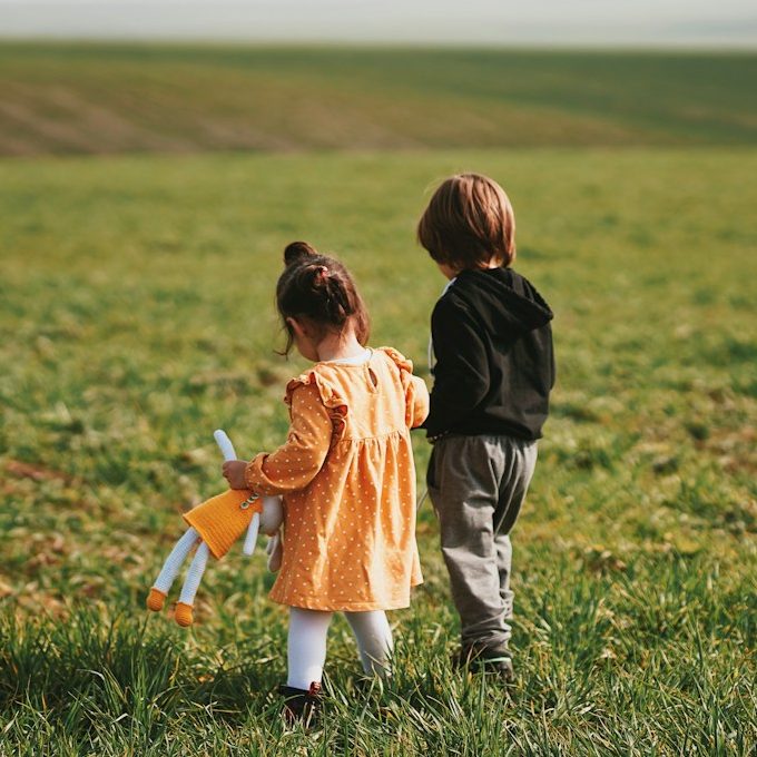 Zwei Kinder sitzen im Grünen, eines zeichnet in ein Heft, das andere beobachtet.
