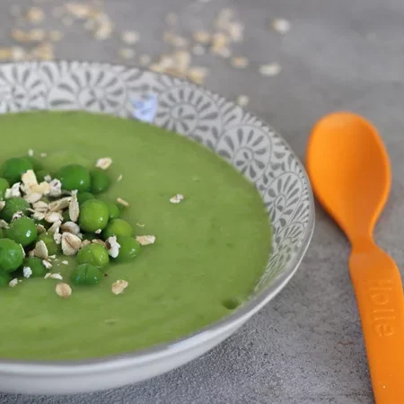 Erbsencremesuppe mit Haferflocken, garniert mit grünen Erbsen in einer dekorativen Schale.