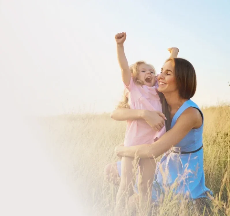 Eine Mutter umarmt ihr fröhliches Kind in einem Feld unter blauem Himmel.