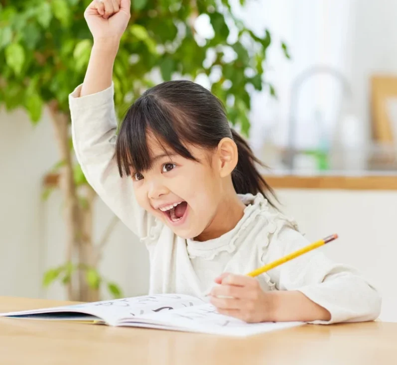 Ein fröhliches Kind mit Stift, das beim Zeichnen begeistert die Hand hebt.