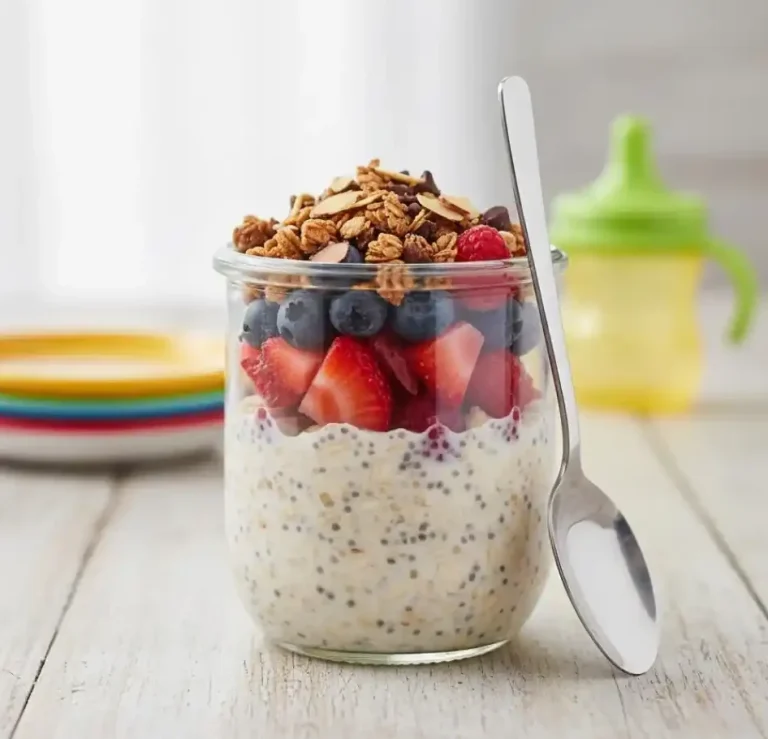 Haferflocken mit Beeren und Granola in einem Glas, daneben ein Löffel und Farbige Teller.