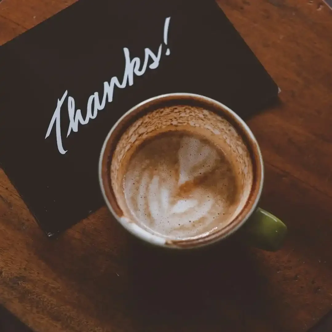 Tasse mit Kaffee und kunstvollem Milchschaum, daneben eine Karte mit „Danke!“.