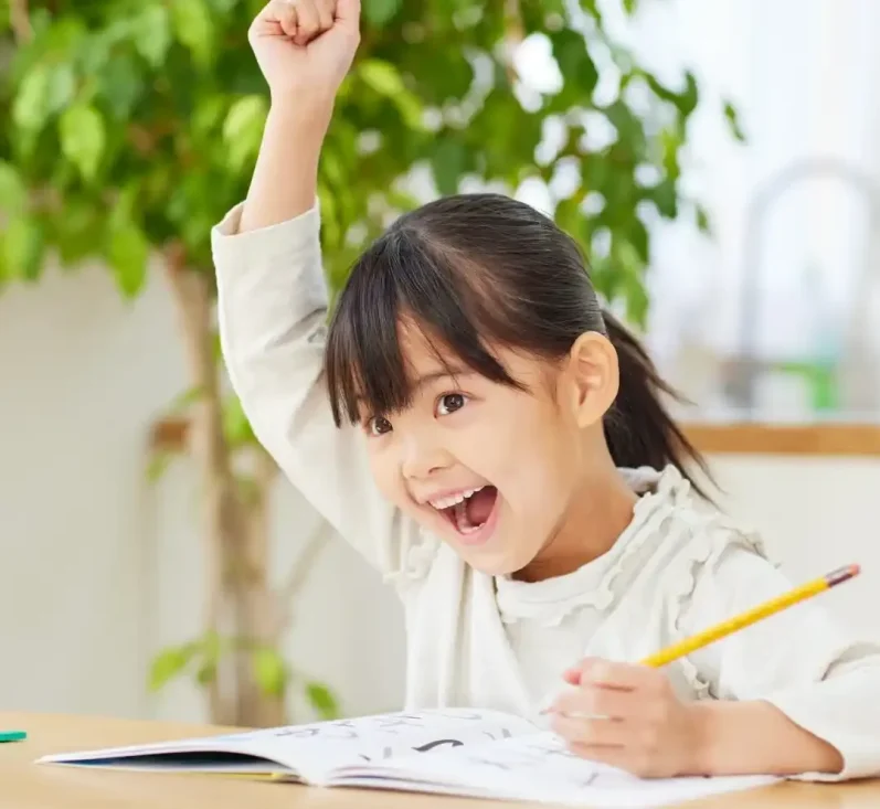 Ein fröhliches Kind mit Stift, das beim Zeichnen begeistert die Hand hebt.