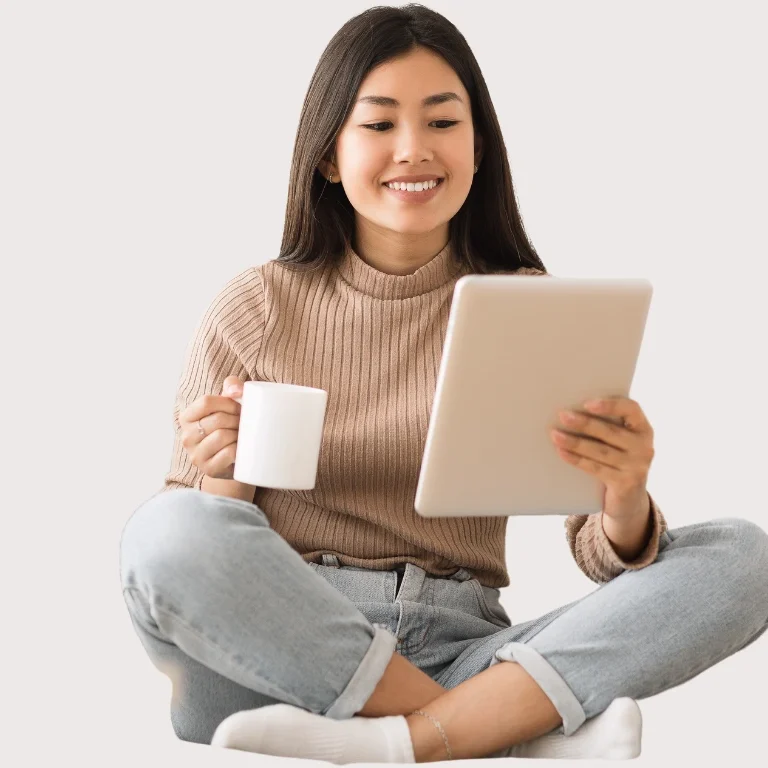 Frau sitzt mit Tablet und Kaffeetasse, lächelnd und in entspannter Haltung.