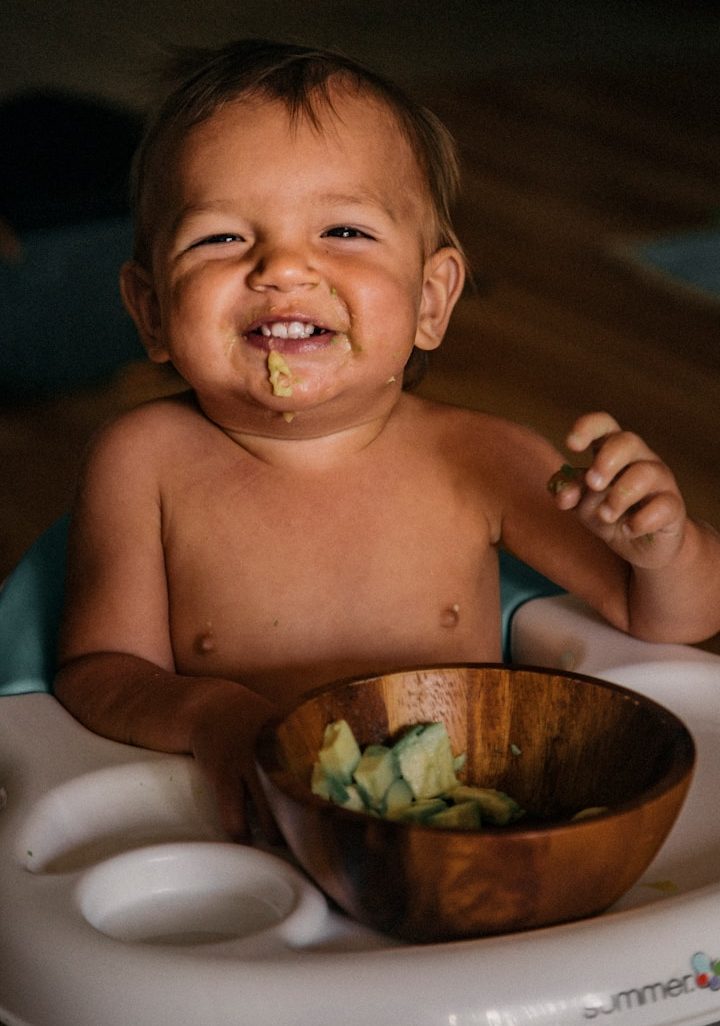 Lächelndes Kleinkind sitzt mit einem Holzschüssel voll Essen.