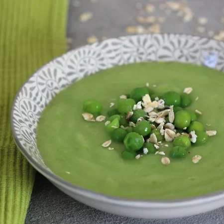 Grüne Erbsensuppe mit frischen Erbsen und Haferflocken in einer dekorativen Schüssel.