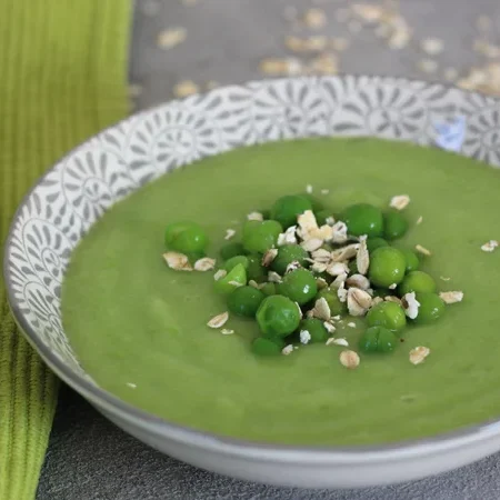 Grüne Erbsensuppe in einer dekorativen Schüssel, garniert mit Erbsen und Haferflocken.