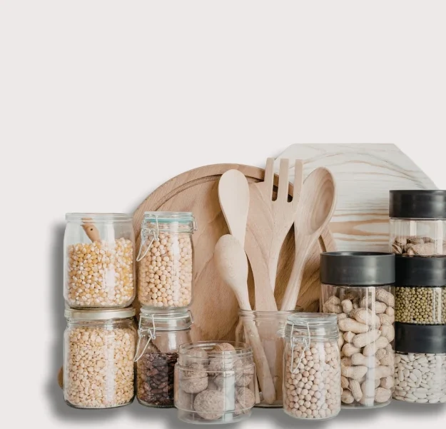 Verschiedene Nahrungsgemüse in Gläsern und Holzutensilien auf einem hellen Hintergrund.