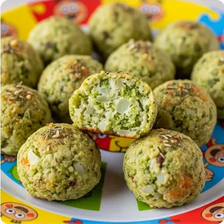 Grüne Bällchen aus Gemüse mit Käsefüllung, auf einem bunten Teller angerichtet.